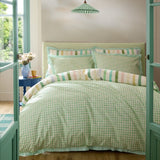 A bed dressed in a light green and white gingham duvet cover and matching pillows, styled in a bedroom with teal doors, a blue side table, and hanging green-and-white lamps.